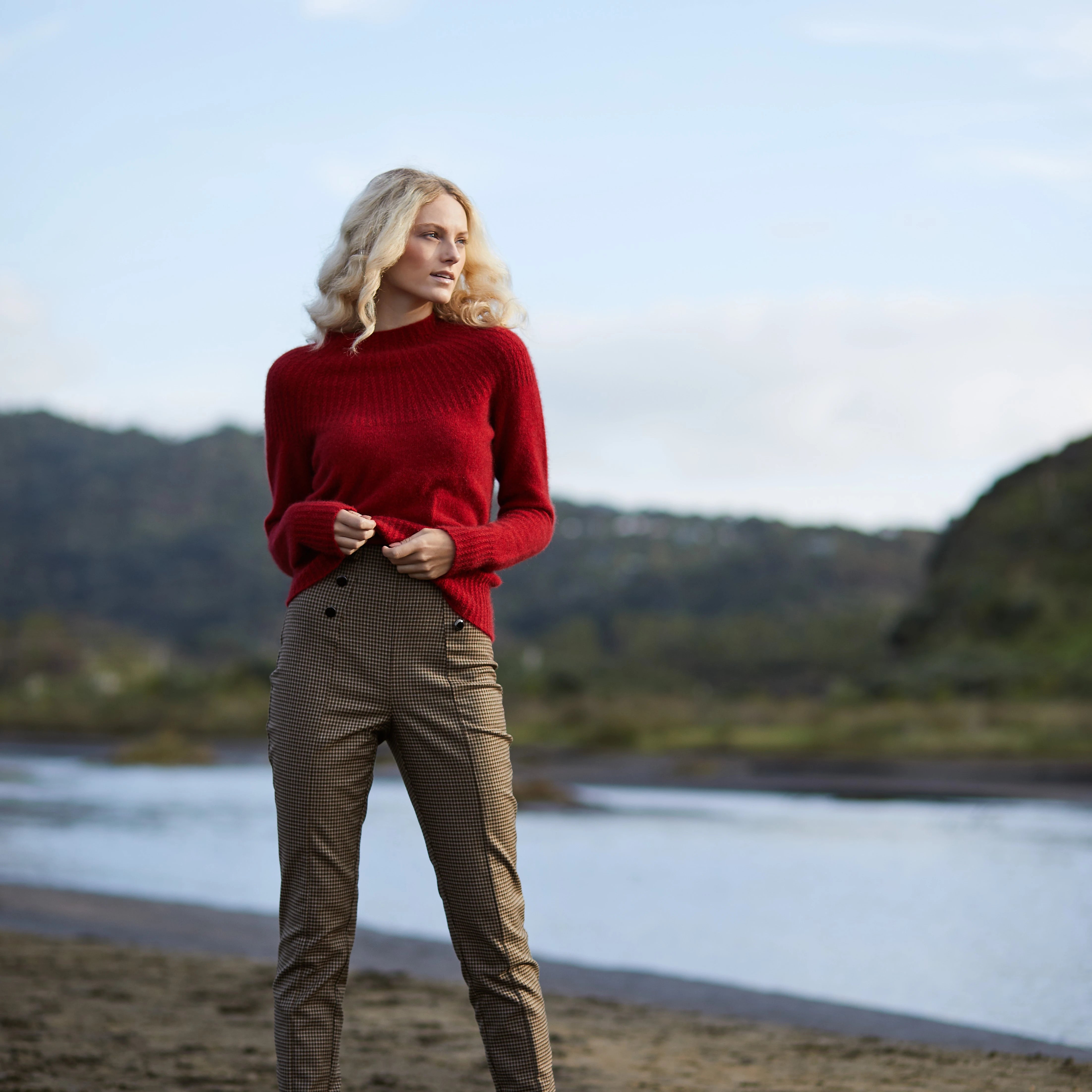 Blond woman carrying a red Merino sweater NZ produced by  MacDonald